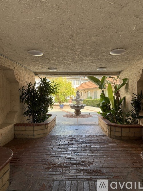A hallway with a brick floor leads to a courtyard with a fountain.