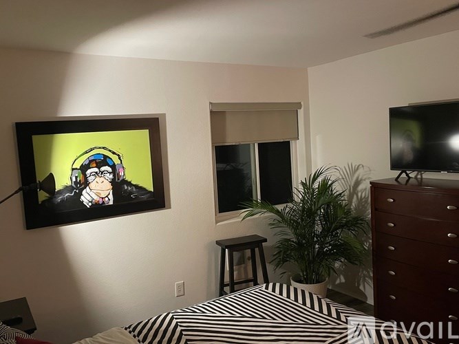 A bedroom with a bed, a painting, a plant, and a TV.