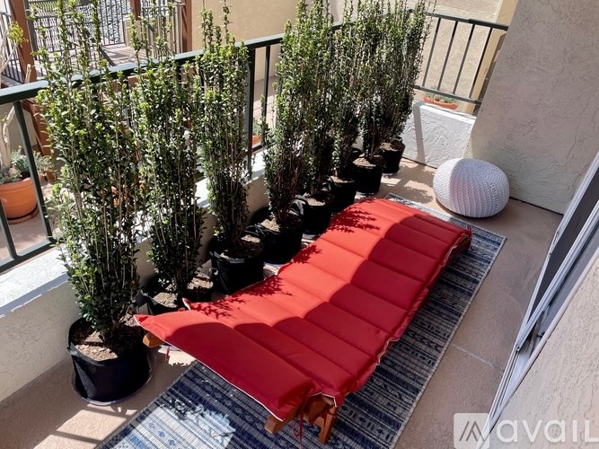 A red mattress is on a balcony with plants on either side.
