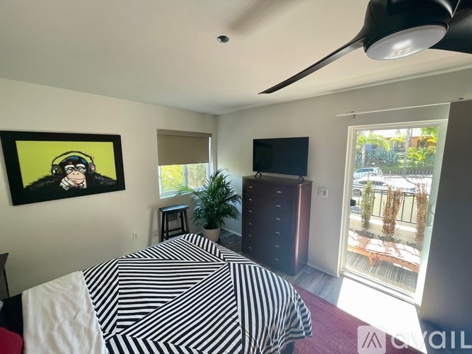 A bedroom with a bed, a television, and a painting of a person wearing headphones.