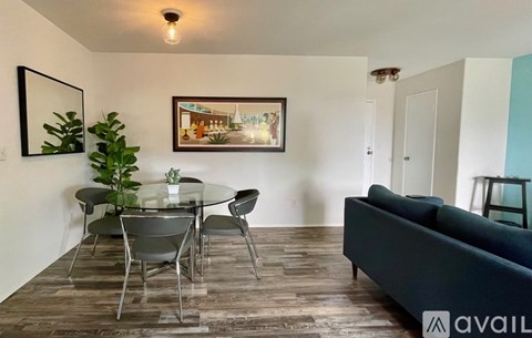 A living room with a glass table and chairs, a couch, and a painting on the wall.