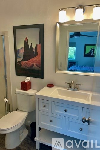 A bathroom with a toilet, sink, and a framed picture of a cityscape.