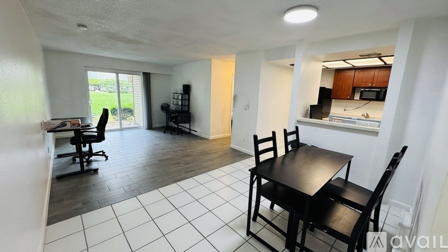 A black dining table with four chairs is in a white tiled room.