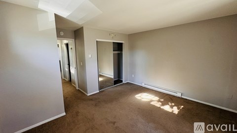 A room with a carpeted floor and a white wall with a door and a mirror.