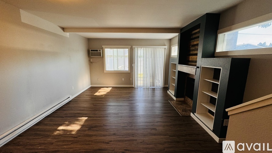 A spacious room with wooden flooring and a window with blinds.