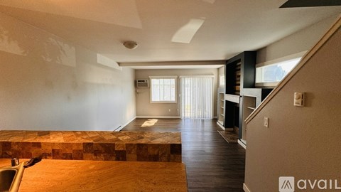 A spacious room with wooden flooring and a window with blinds.