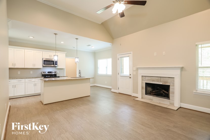 A spacious living room with a fireplace and a kitchen area in the background.