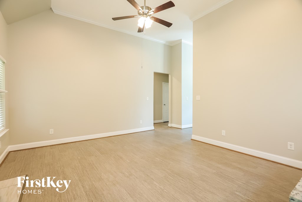 A spacious room with a ceiling fan and light fixture, and a doorway leading to another room.