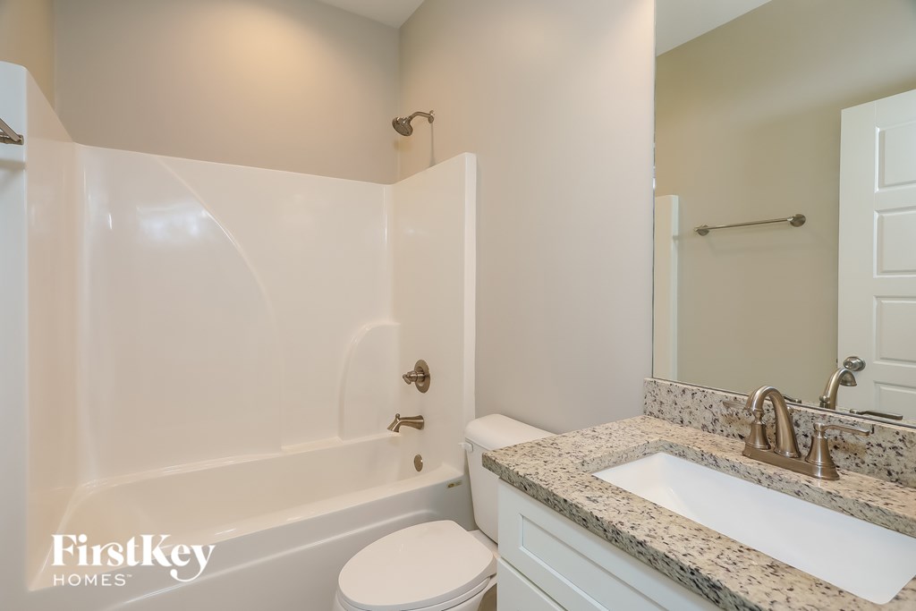 A white bathroom with a marble counter top and a white toilet.