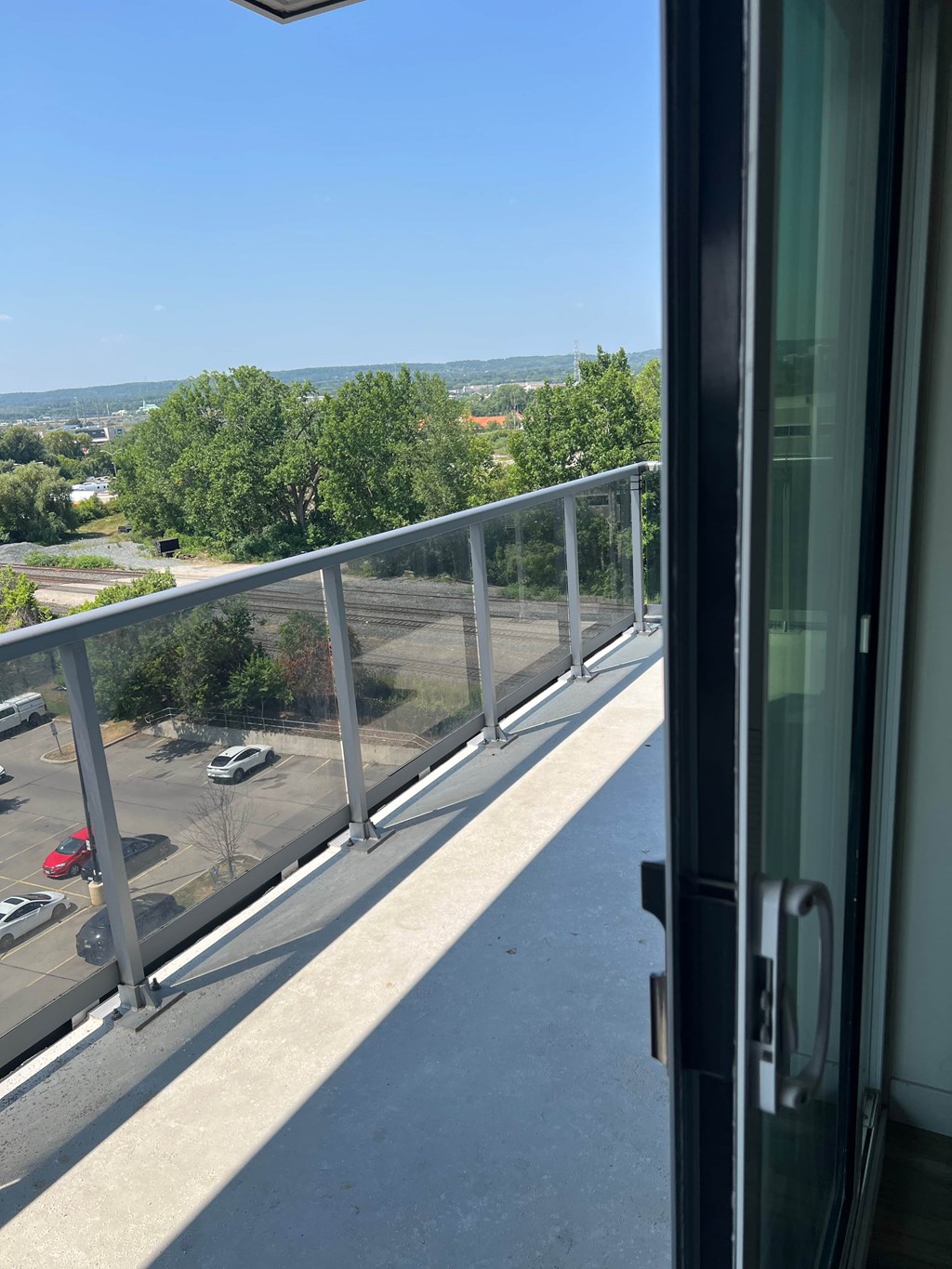 A balcony with a view of a parking lot and trees.