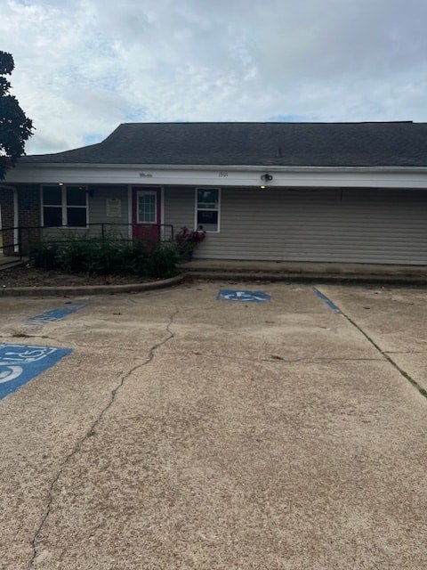 A cracked parking lot in front of a grey building with a red door.