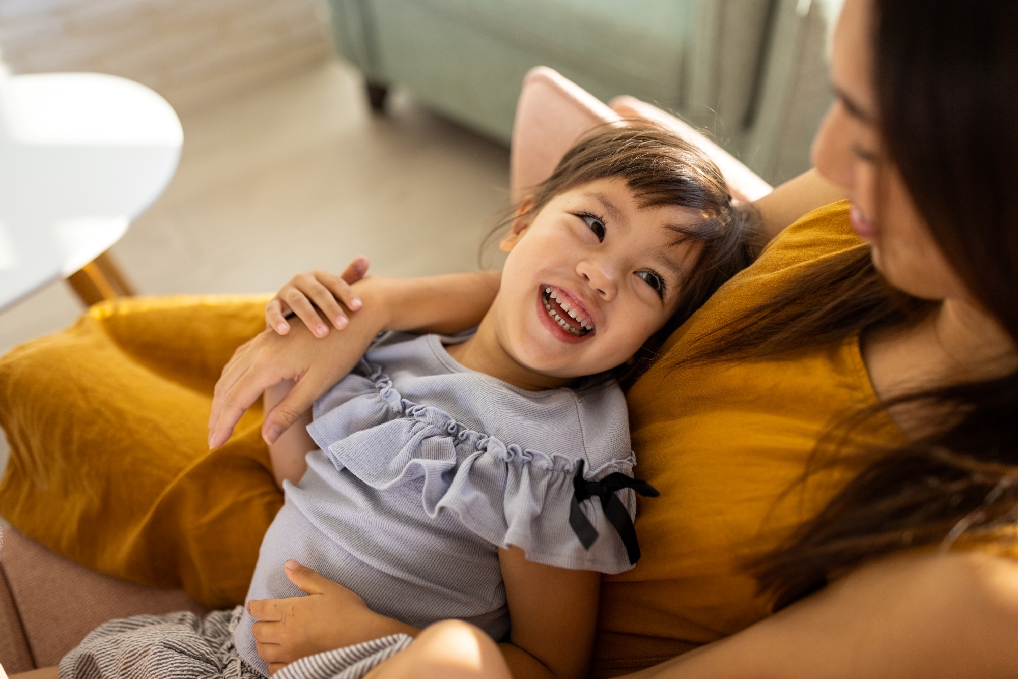 mother and daughter laughing on a couch at home