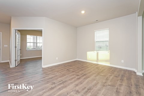 A spacious empty room with wooden flooring and a doorway leading to another room.