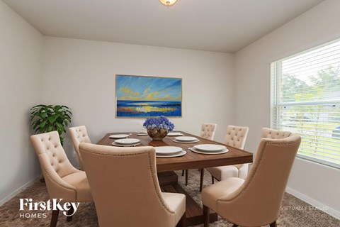A dining room with a wooden table and chairs, a painting on the wall, and a potted plant on the left.