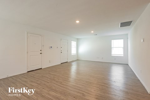 A spacious room with wooden flooring and white walls, with a door on the left and two windows on the right.