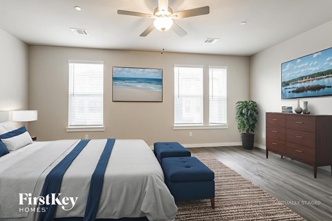 A bedroom with a bed, a bench, a ceiling fan, and a painting on the wall.