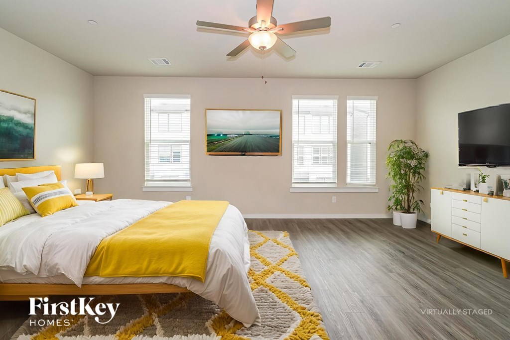 A bedroom with a bed, a ceiling fan, and a painting on the wall.
