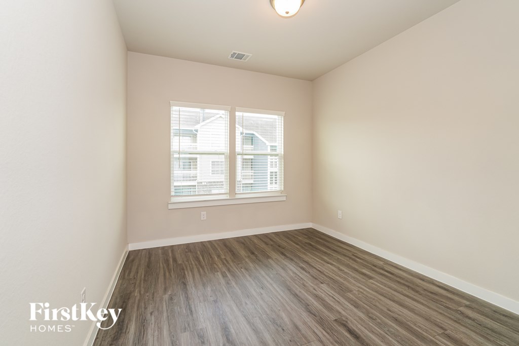 A room with wooden flooring and a window showing a view of a building outside.