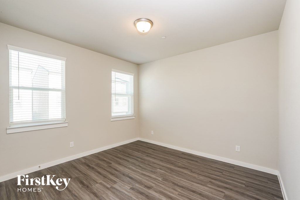 A room with wooden flooring and two windows.