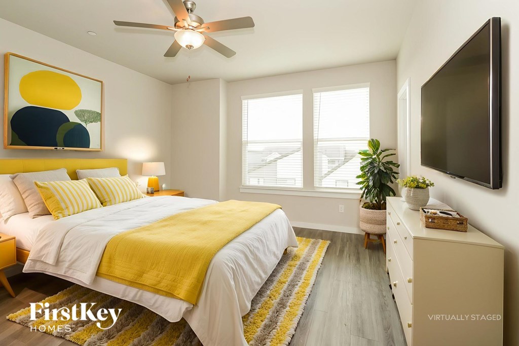 A bedroom with a bed, a ceiling fan, a dresser, and a painting on the wall.