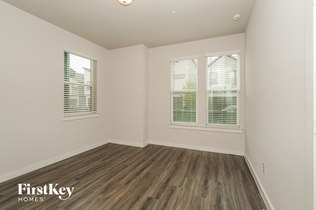A room with wooden flooring and two windows with blinds.