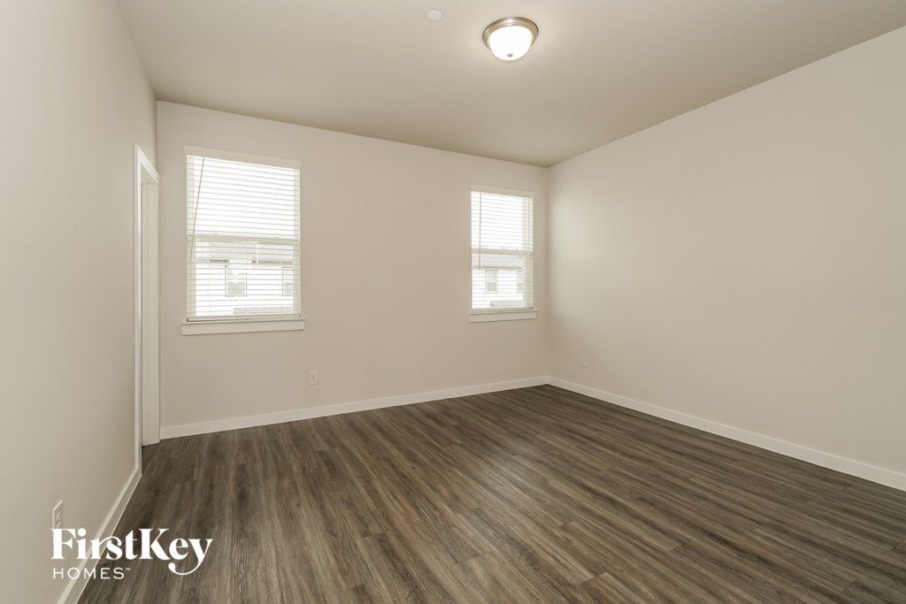 A room with wooden flooring and two windows.