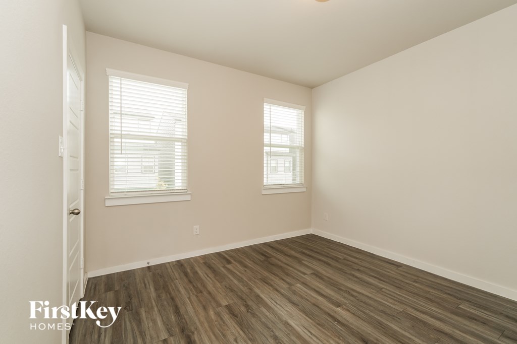 A room with wooden flooring and two windows.