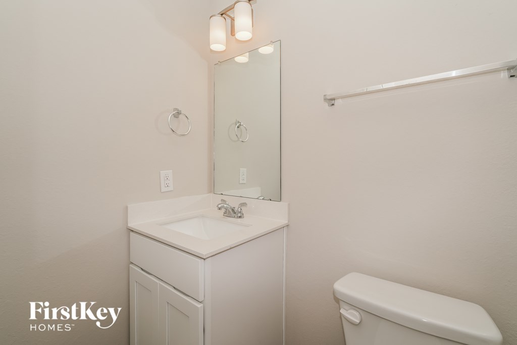 A white bathroom with a sink, mirror, and toilet.