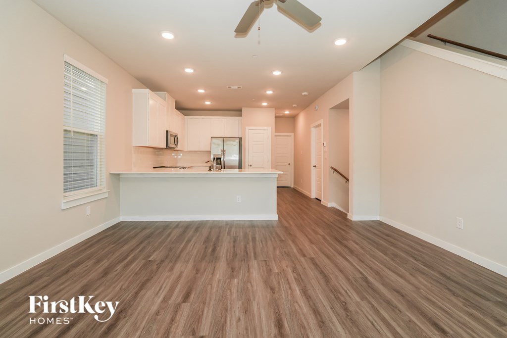 A spacious room with wooden flooring and a kitchen area in the background.
