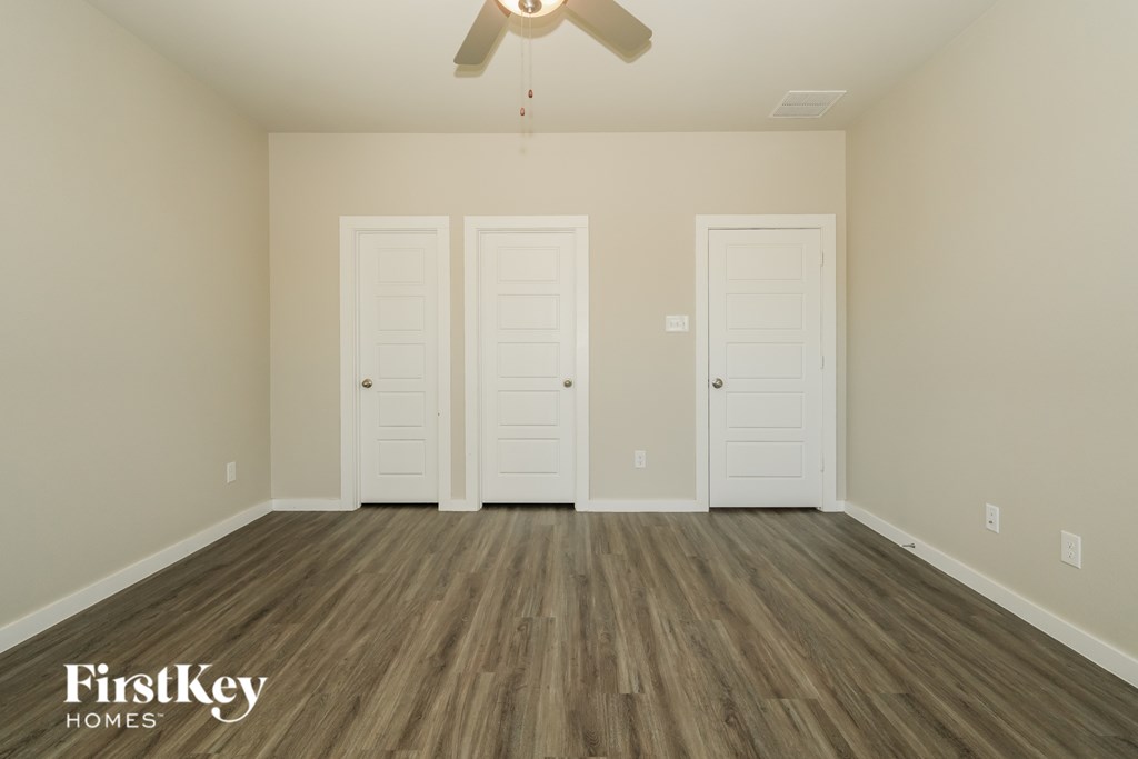 A room with wood flooring and three white doors.