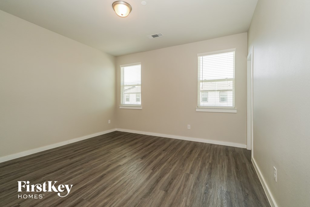 A room with wooden flooring and two windows.