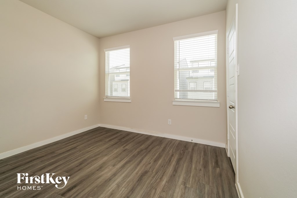 A room with wooden flooring and two windows.