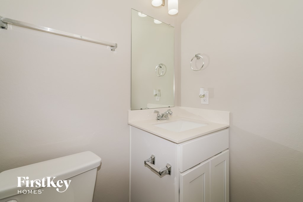 A white bathroom with a toilet, sink and mirror.