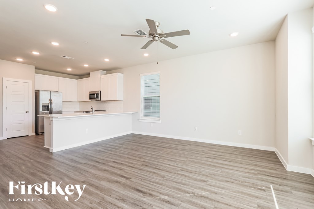 A spacious kitchen and living room with a ceiling fan and lighting.