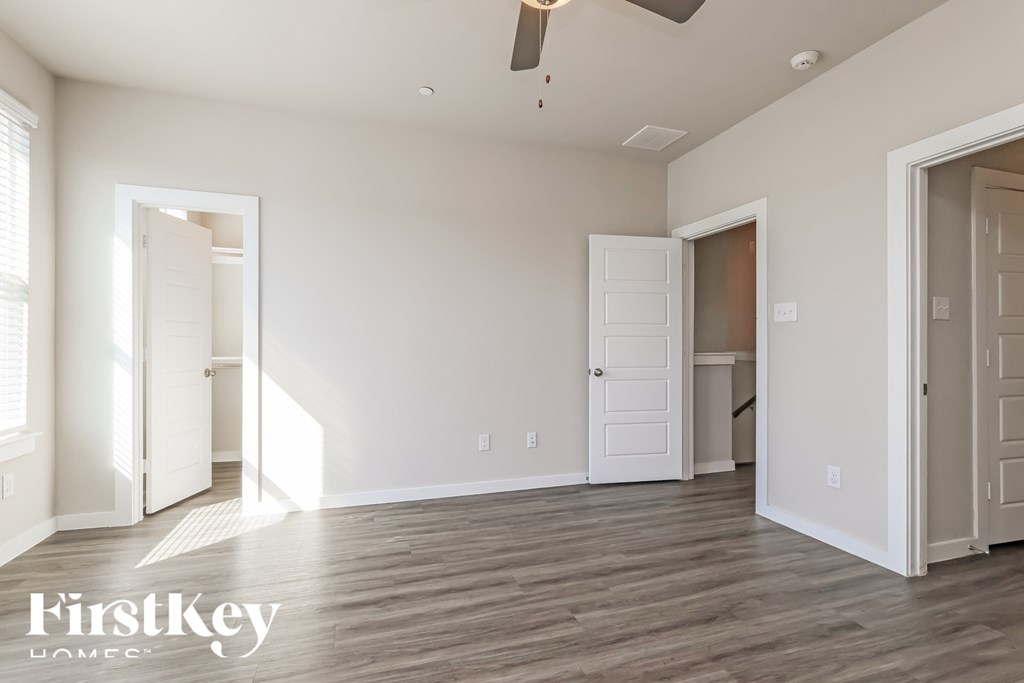 A spacious room with wooden flooring and a ceiling fan, with a FirstKey Homes logo in the corner.