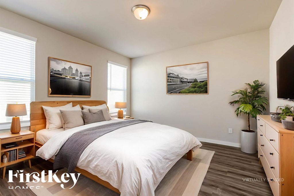 A bedroom with a large bed, a nightstand with a lamp, and two pictures on the wall.