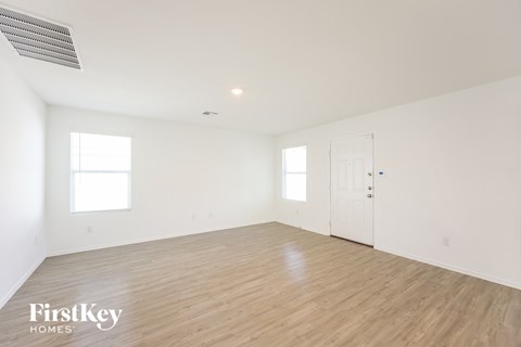 A spacious room with wooden flooring and white walls, with a door on the right side.