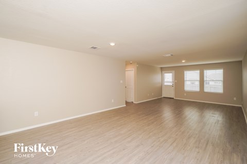 A spacious room with wooden flooring and white walls, with a window on the right wall.
