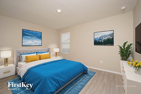 A bedroom with a blue bedspread and a painting of a mountain scene on the wall.