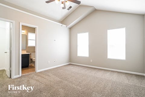 A spacious room with a ceiling fan and three windows.