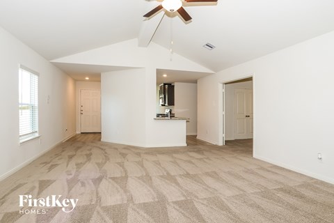 A spacious, empty room with a fan and carpeted floor.