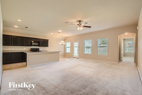 A spacious living room with a kitchen area in the background and a carpet on the floor.
