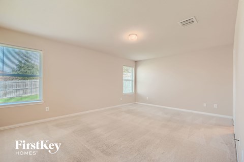 A room with a carpeted floor and a window showing a view of a fence and trees.