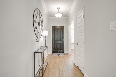 A hallway with a clock on the wall and a door at the end.