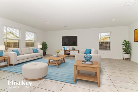 A living room with a white couch, a white chair, a white ottoman, a wooden coffee table, a blue rug, a flat screen TV, and a potted plant.