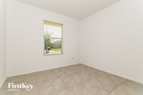 A room with a window showing a view of a house and trees outside.