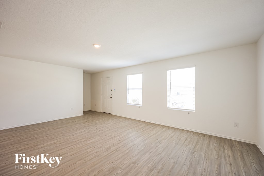 A spacious room with wooden flooring and two windows.