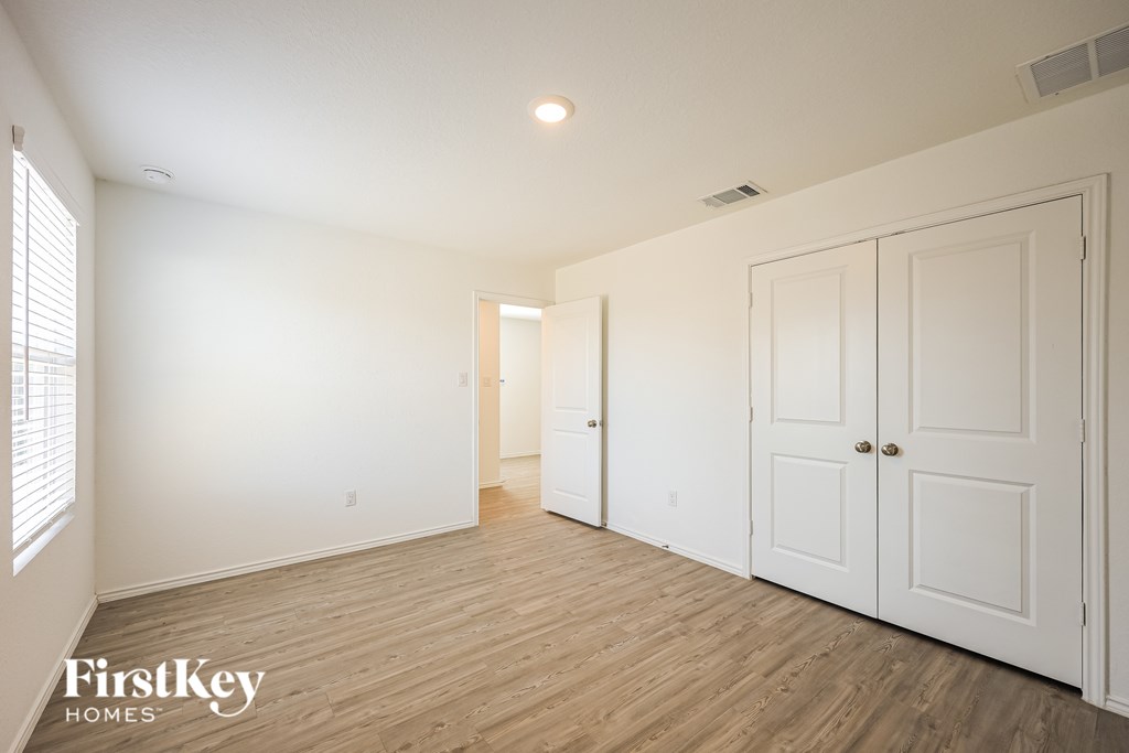 A room with wooden floors and white walls, with a door on the right and a window on the left.