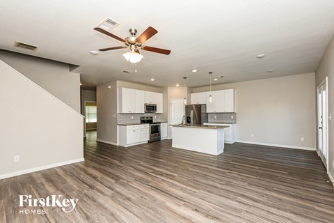 A spacious kitchen and living room with a ceiling fan and hardwood floors.