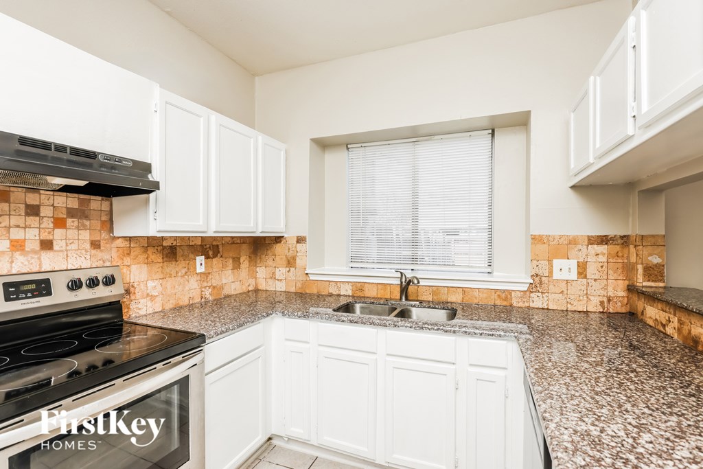 A kitchen with a tiled backsplash and a stove top oven.